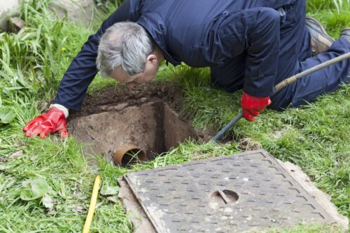 Drain being cleared by worker in navy overalls.